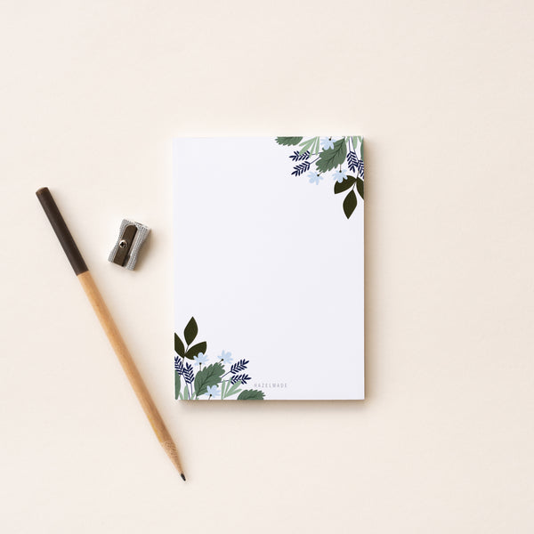 A single 4” by 5.5” small notepad with 50 tear-off sheets and an illustration of blue flowers and green leaves wrapping the top right and bottom left corner while the rest of the notepad is blank.