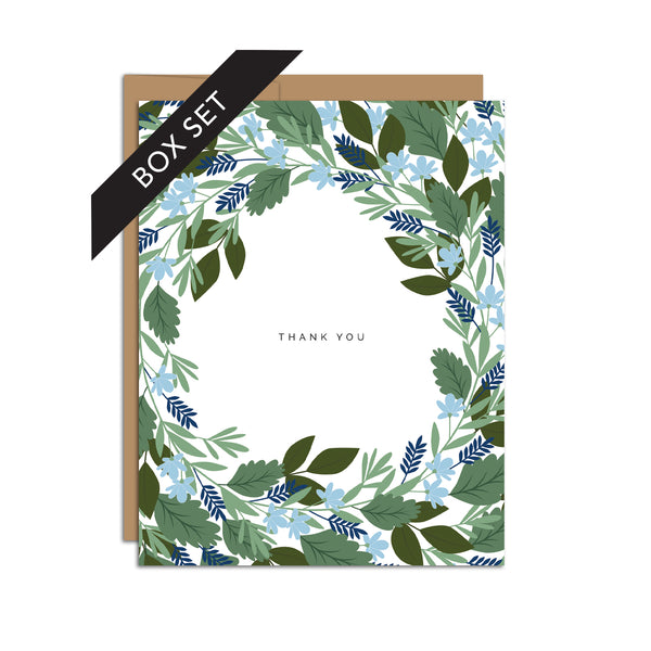 Box set of 8 folded A2 greeting cards with envelopes with an illustration   of blue flowers and green leaves circling/bordering all edges of the card. In the center is text that states "Thank You".