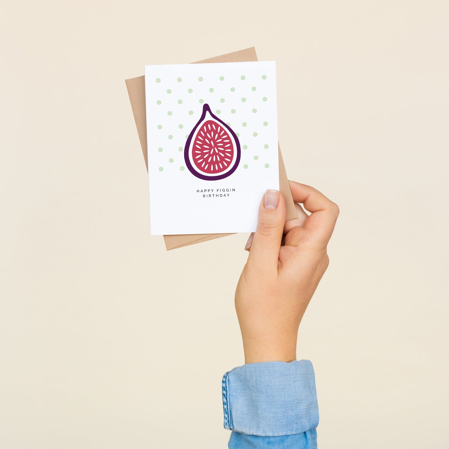 A hand holding the Happy Figgin Birthday greeting card and envelope showing the hand-illustrated fig design