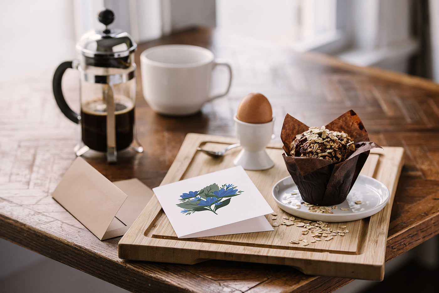 Hand-illustrated greeting card with envelope beside coffee, a soft-boiled egg, and muffin on a wooden table
