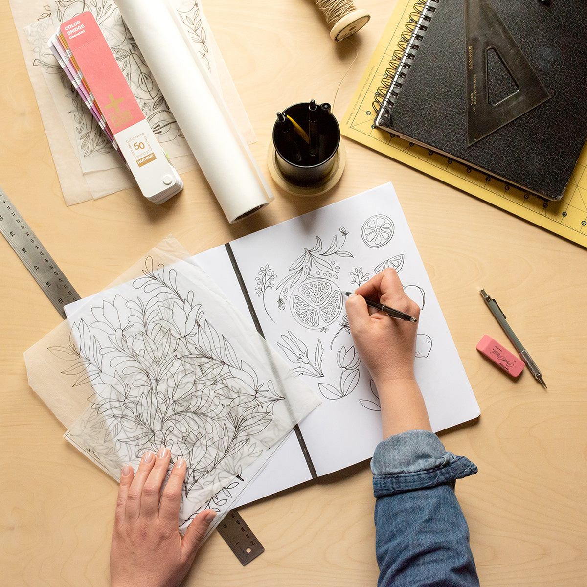 Hand sketching original floral artwork in a notebook on a design workspace