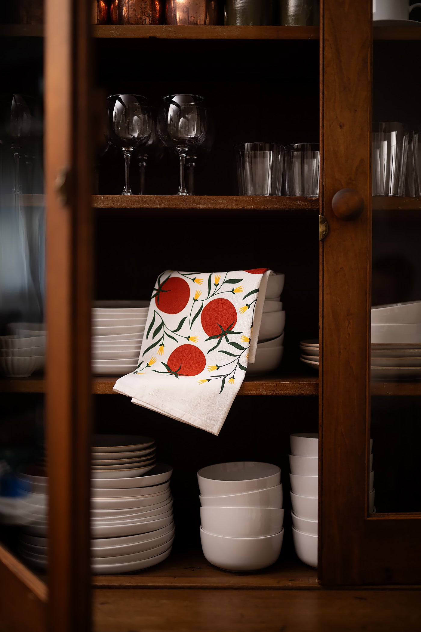 Hand-illustrated cotton tea towel with tomato design displayed in a wooden kitchen cabinet