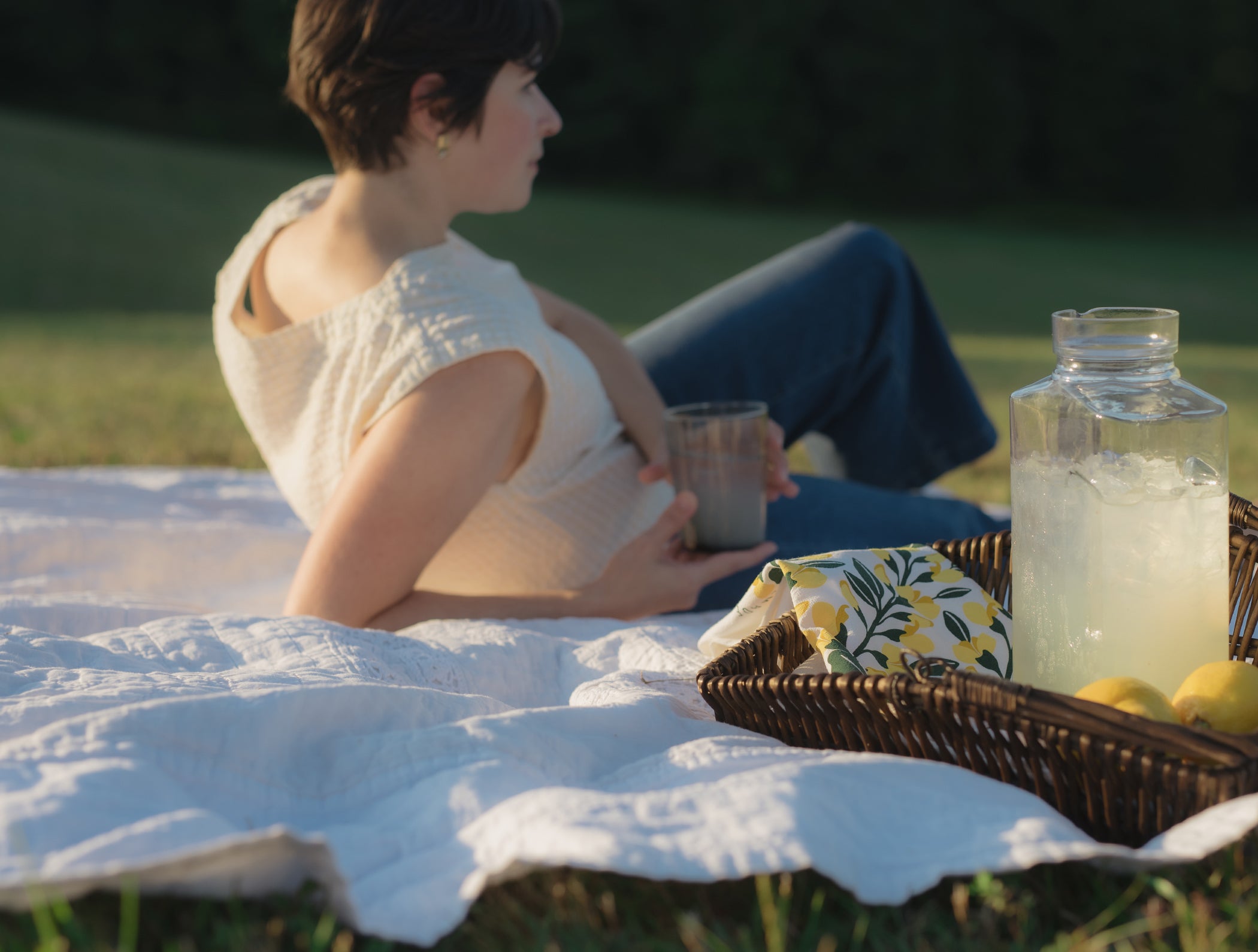 Person relaxing on a picnic blanket beside lemonade and a Hazelmade floral tea towel
