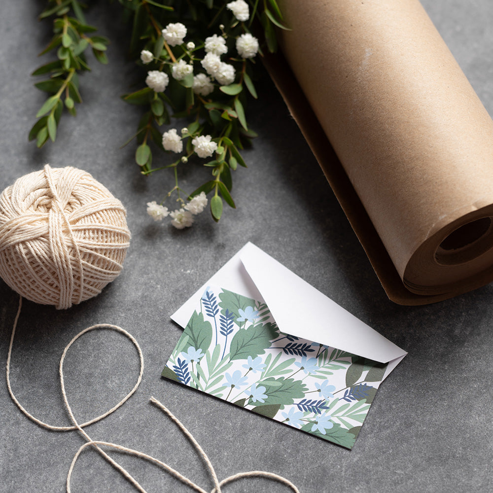 Hand-illustrated mini note card and envelope beside twine, brown wrapping paper, and greenery
