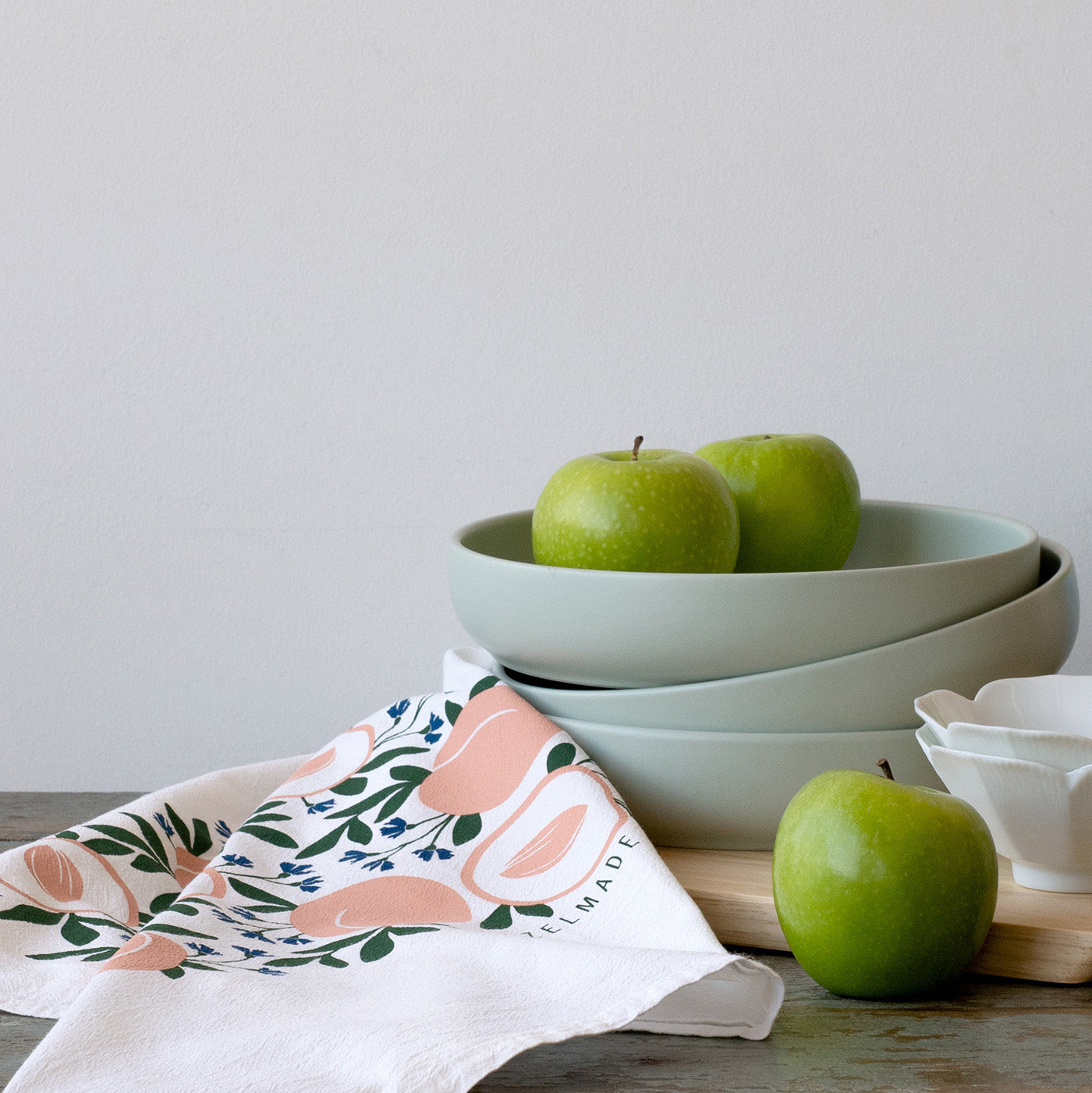 Hazelmade tea towel styled beside stacked bowls and green apples on a tabletop