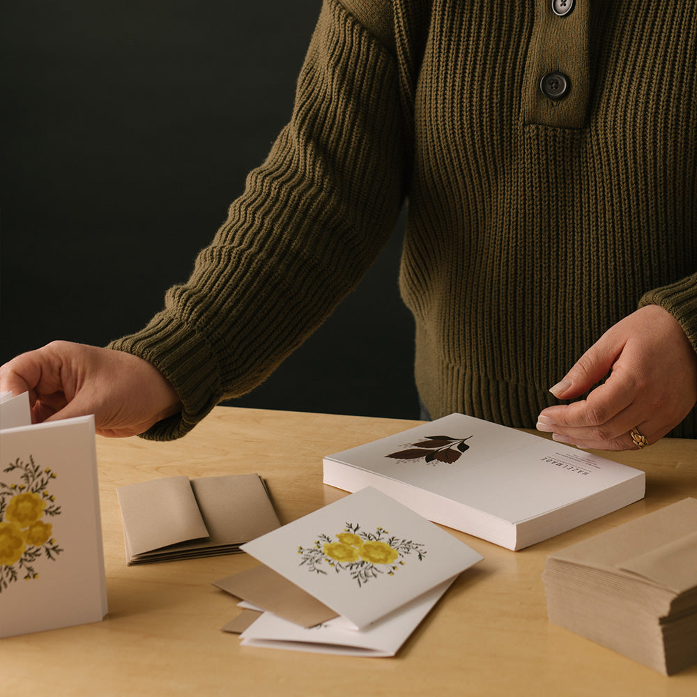 Person arranging hand-illustrated greeting cards and envelopes on a wooden table