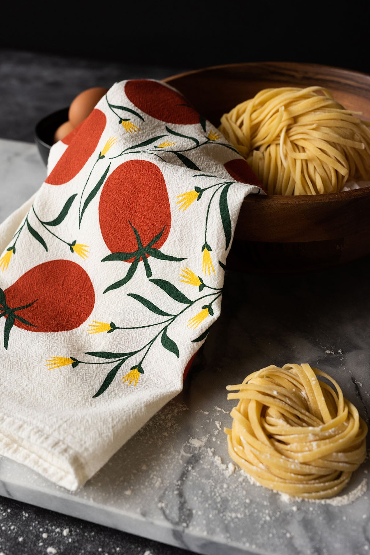 Tomato-patterned Hazelmade tea towel styled with fresh pasta and eggs on a kitchen counter