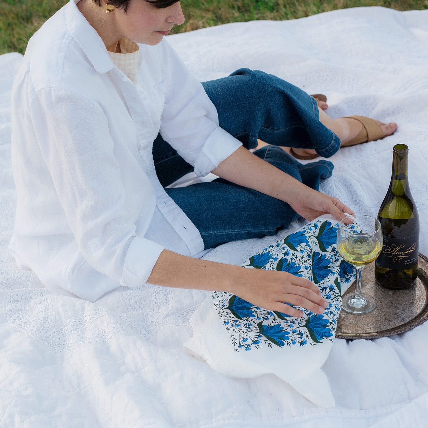 Person sitting on a picnic blanket with a bottle of wine and a Hazelmade floral tea towel
