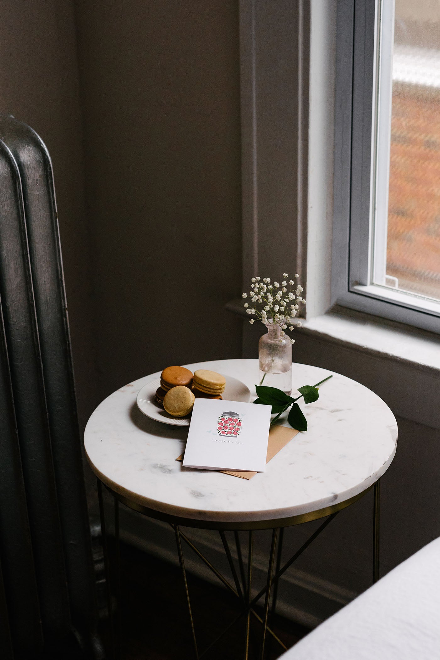Hand-illustrated greeting card with envelope on a marble side table beside macarons and flowers