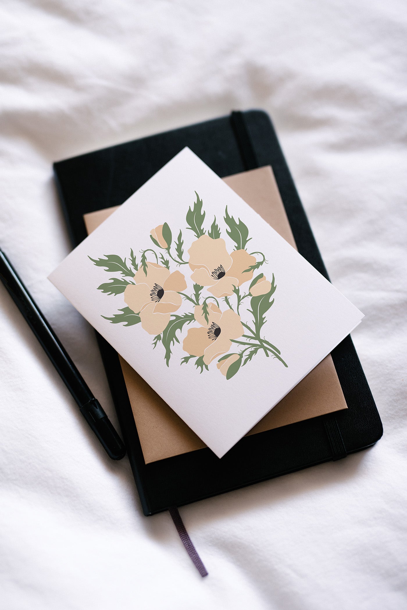 Hand-illustrated floral greeting card with envelope on a black journal beside a pen