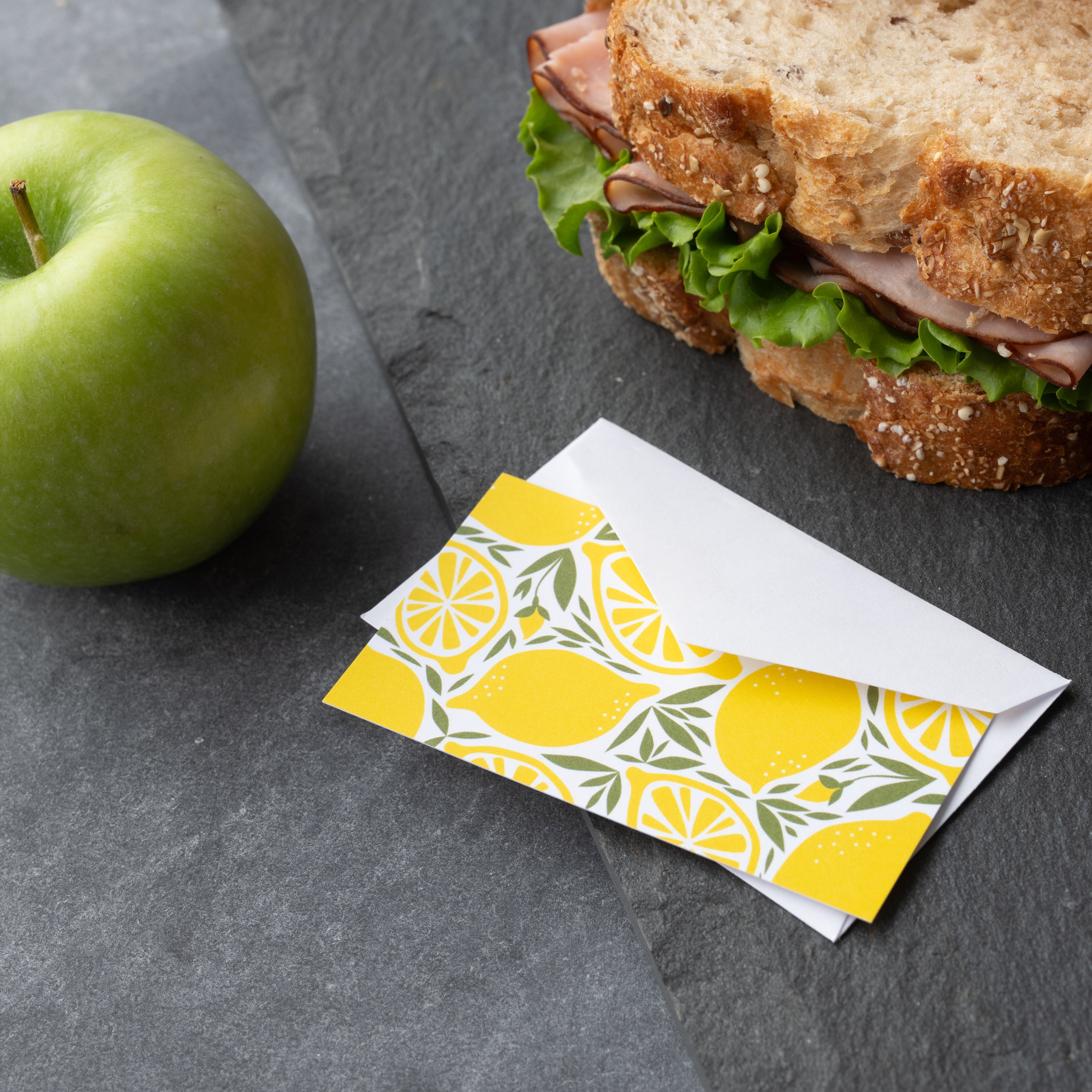 Lemons Mini Note Card styled beside a sandwich and green apple on a dark surface