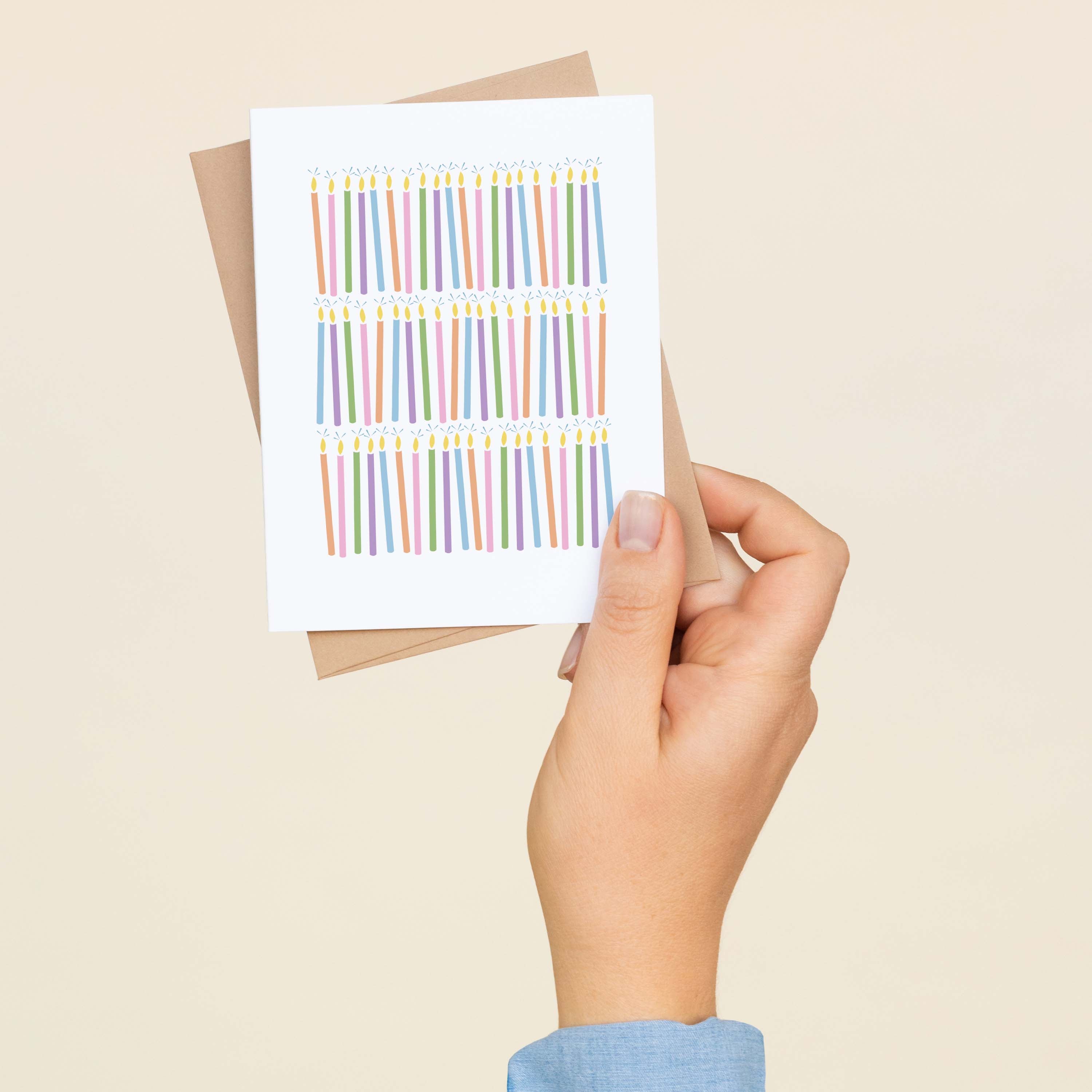 A hand holding a Birthday Candles greeting card and envelope showing the hand-illustrated birthday candle design