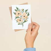 A hand holding a White Windflowers greeting card showing the hand-illustrated white windflower design