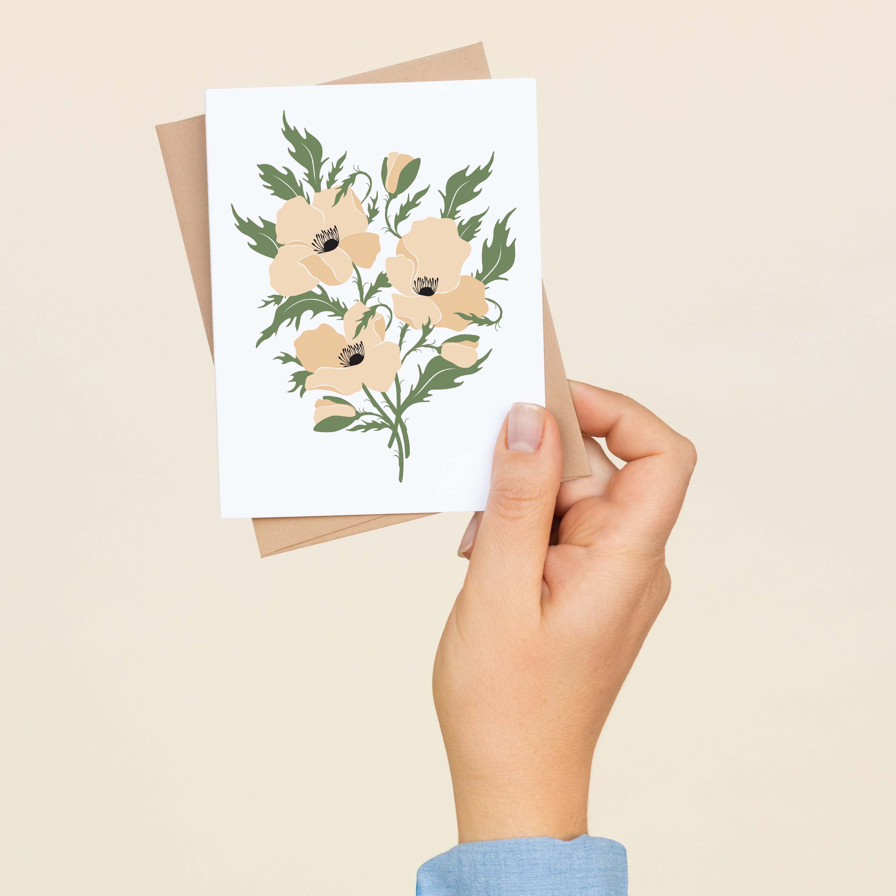 A hand holding a White Windflowers greeting card showing the hand-illustrated white windflower design