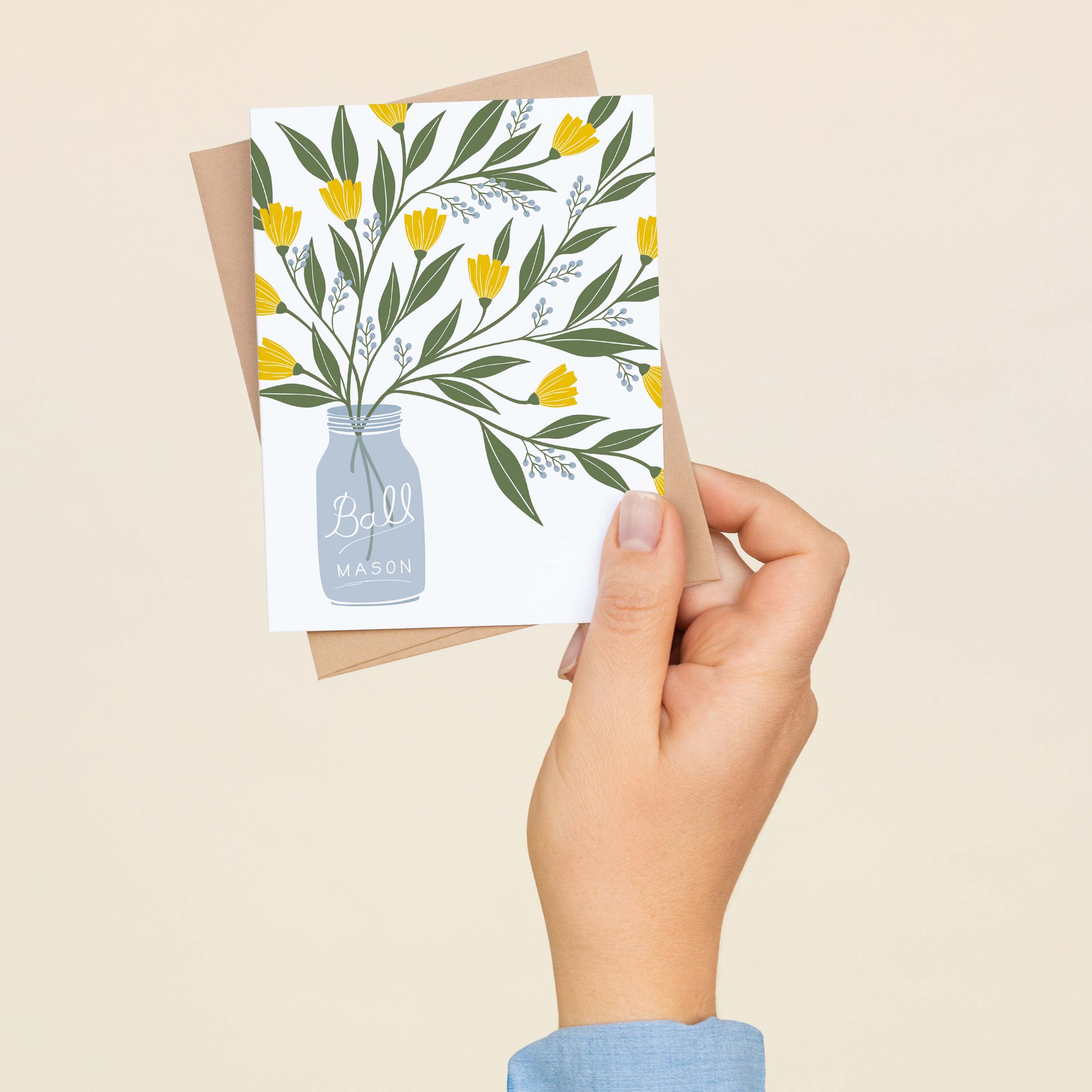 A hand holding a Mason Jar Bouquet greeting card showing the hand-illustrated mason jar floral design