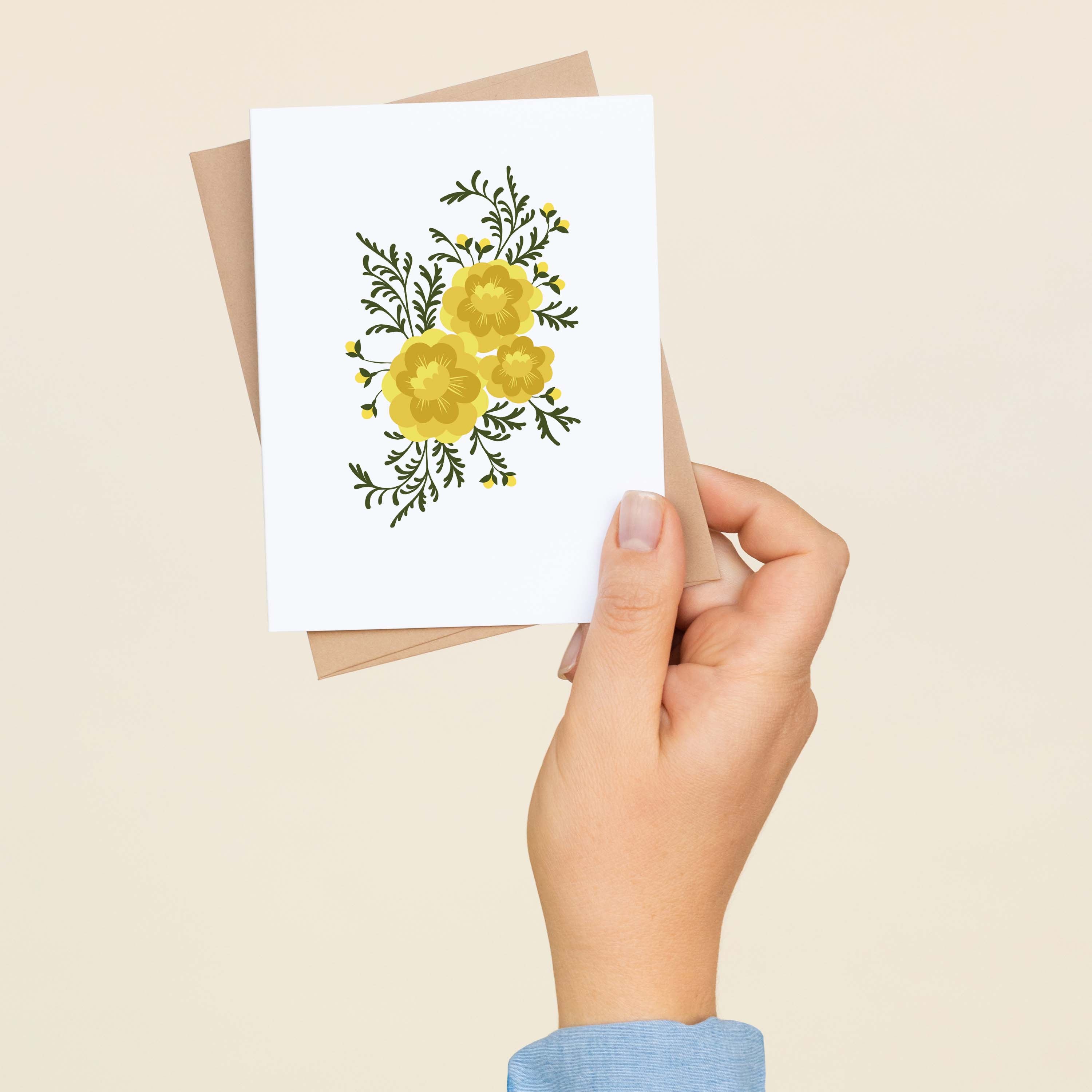 A hand holding a Marigolds greeting card and envelope showing the hand-illustrated yellow marigold design
