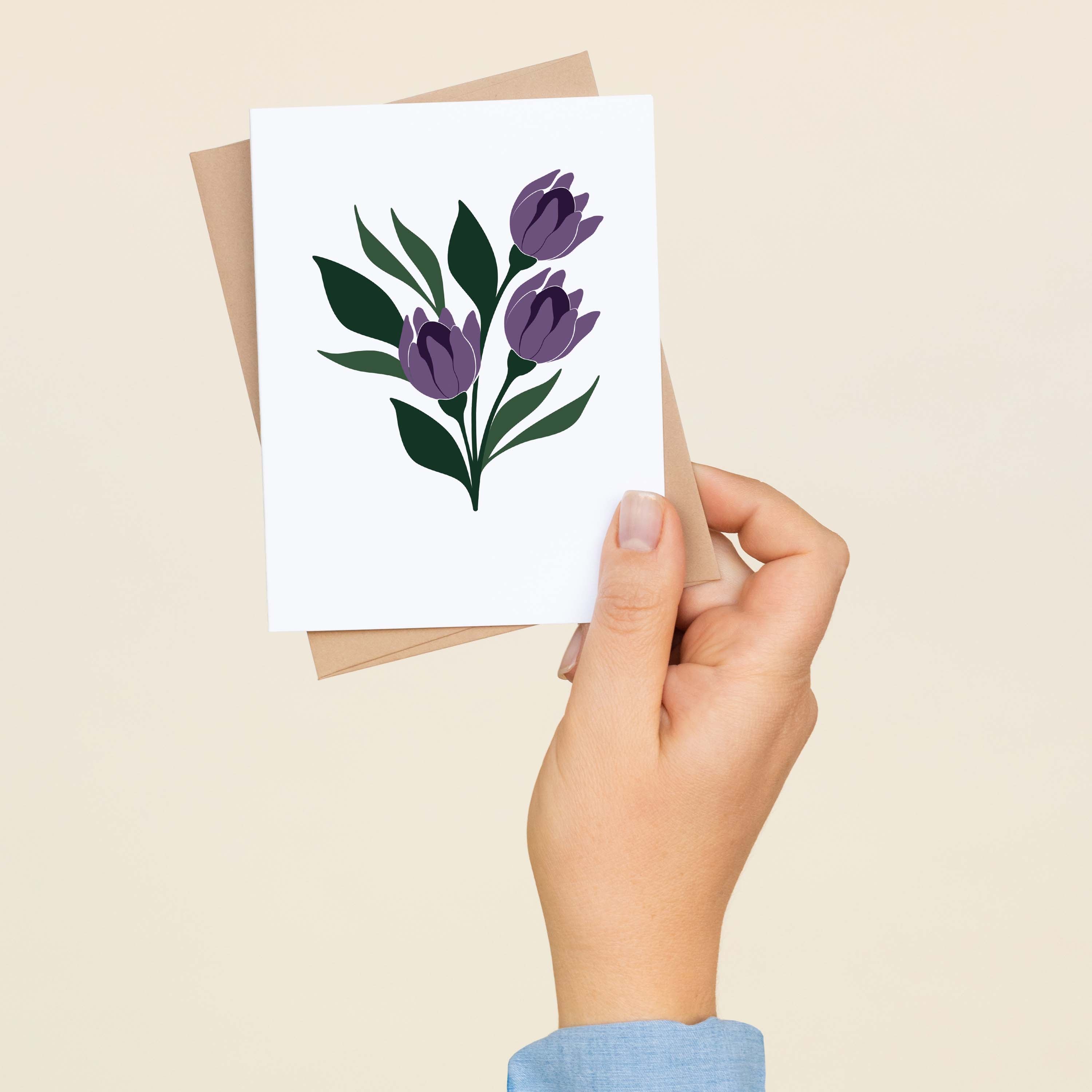A hand holding a Tulips greeting card and envelope showing the hand-illustrated purple tulip design