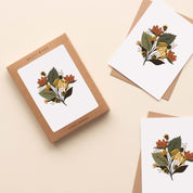 A boxed set of Fall Florals Greeting Cards sitting with two cards and their envelopes featuring a hand-illustrated autumn floral design