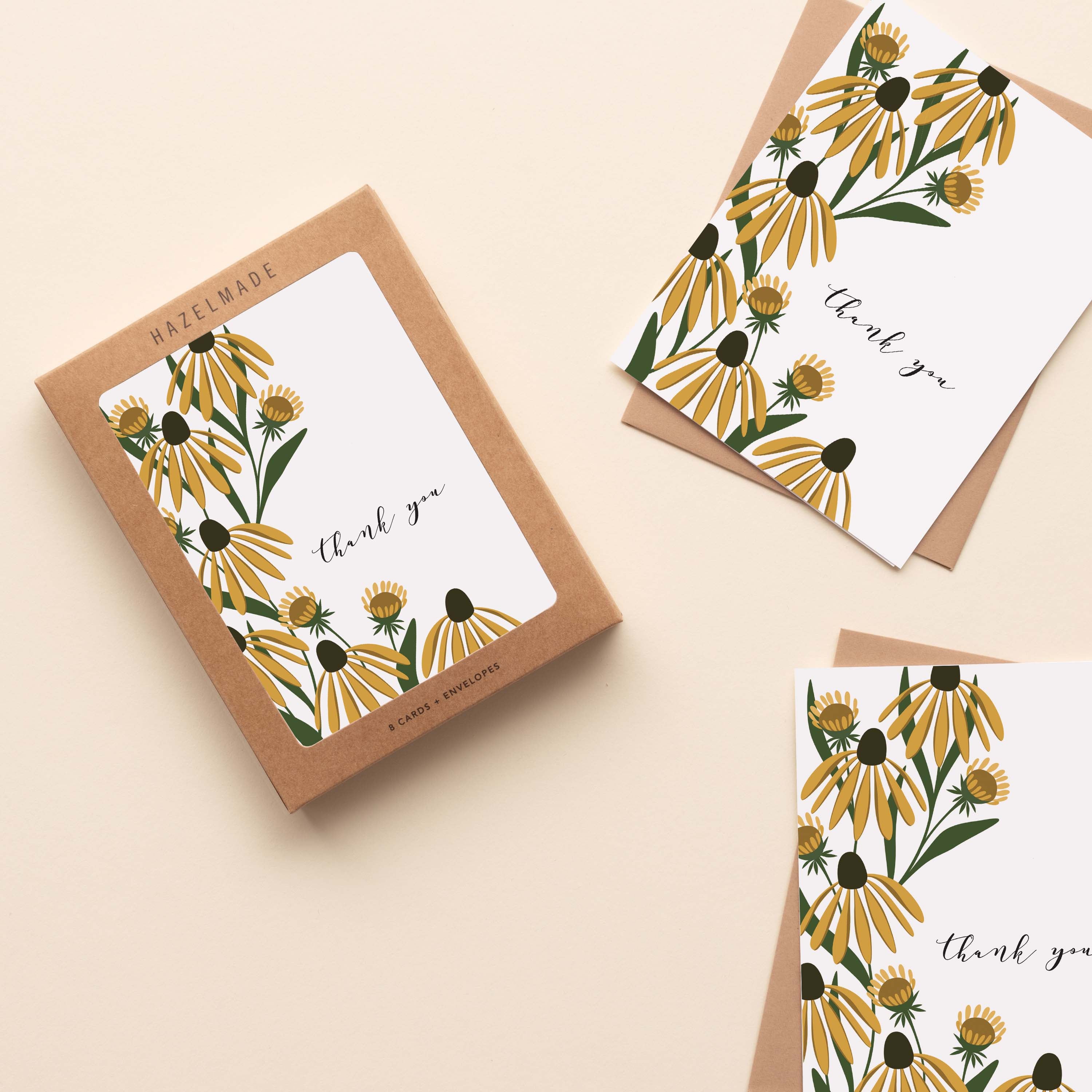 A boxed set of Golden Coneflower Thank You Greeting Cards sitting with two cards and their envelopes featuring a hand-illustrated golden coneflower design