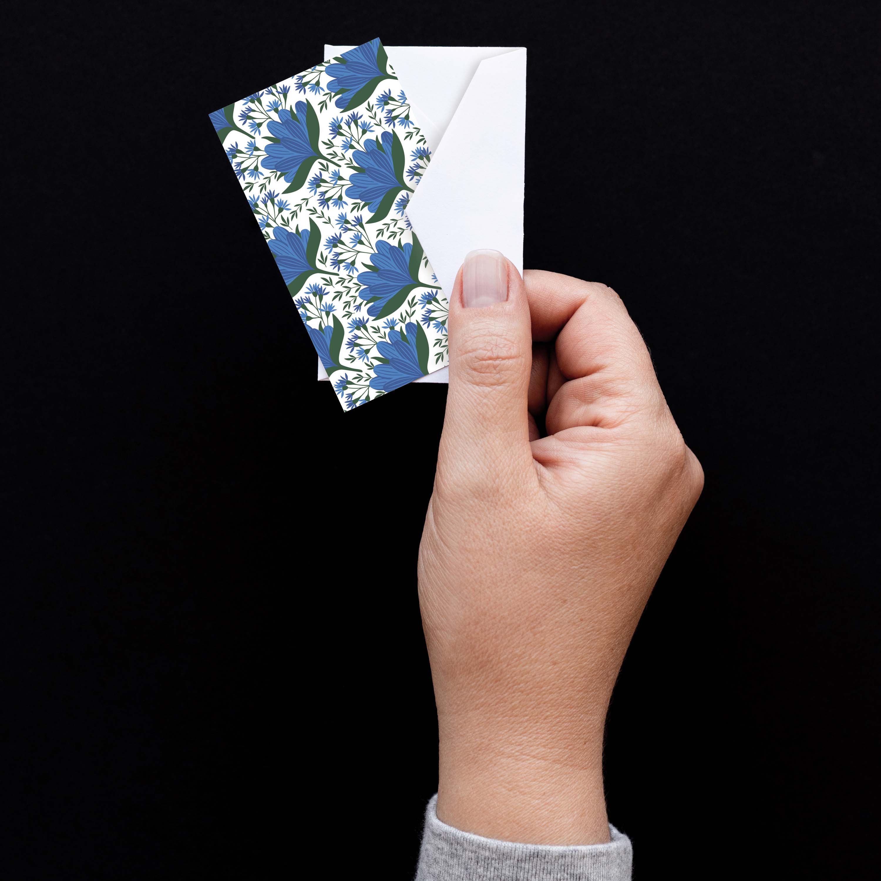 Hand holding a Blue Gentian Mini Note Card with a white envelope against a dark background