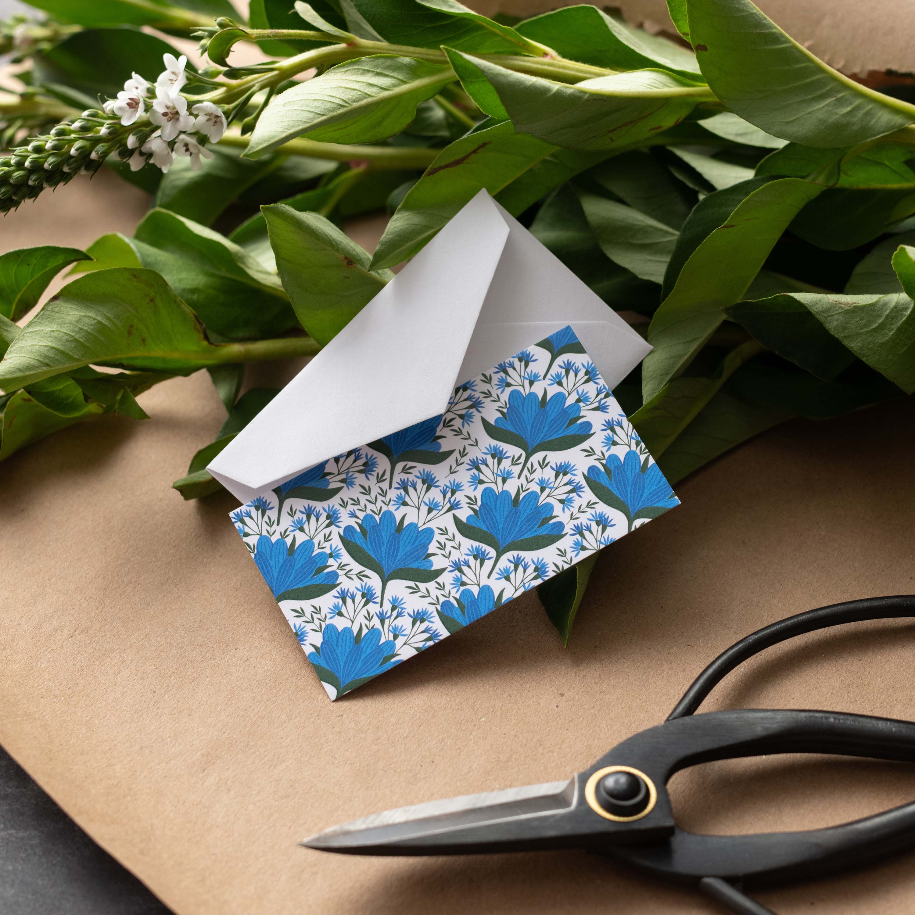 Blue Gentian Mini Note Card styled with a white envelope, greenery, and scissors on kraft paper