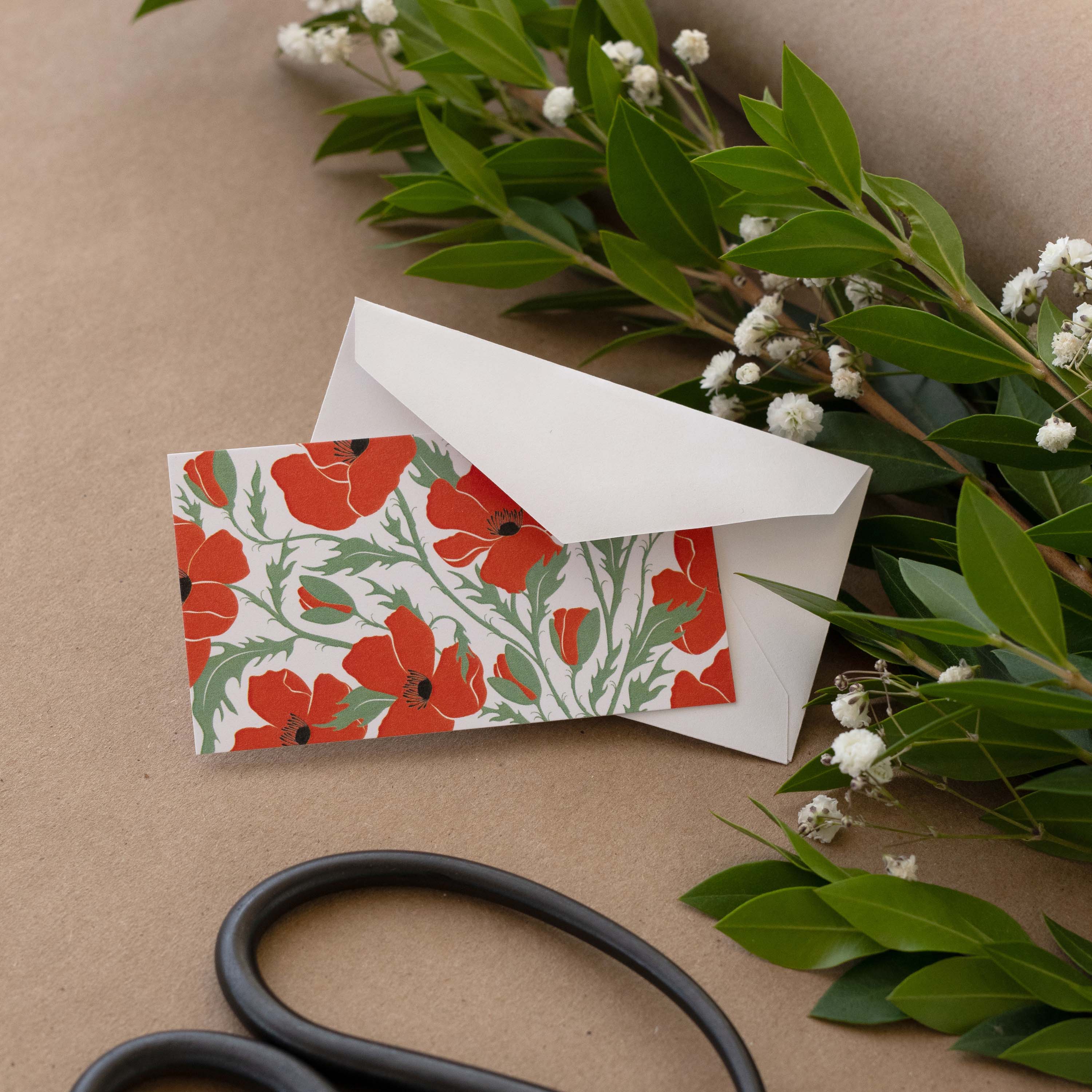 Poppies Mini Note Card styled with a white envelope, greenery, and scissors on kraft paper