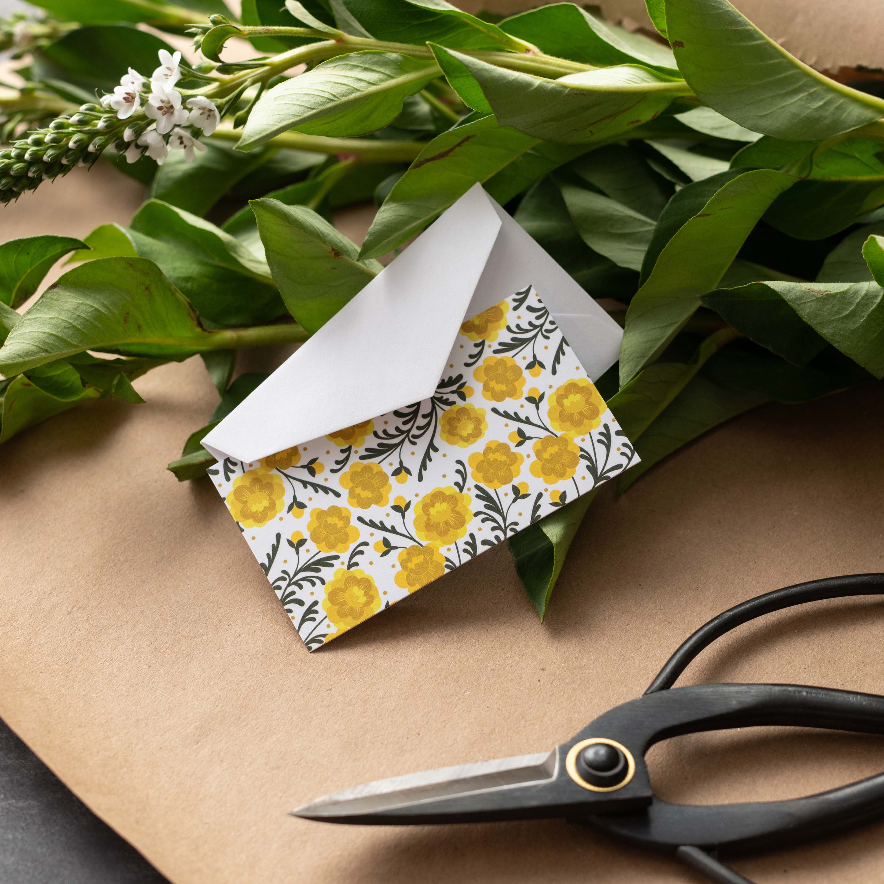 Marigold Mini Note Card styled with a white envelope, greenery, and scissors on kraft paper