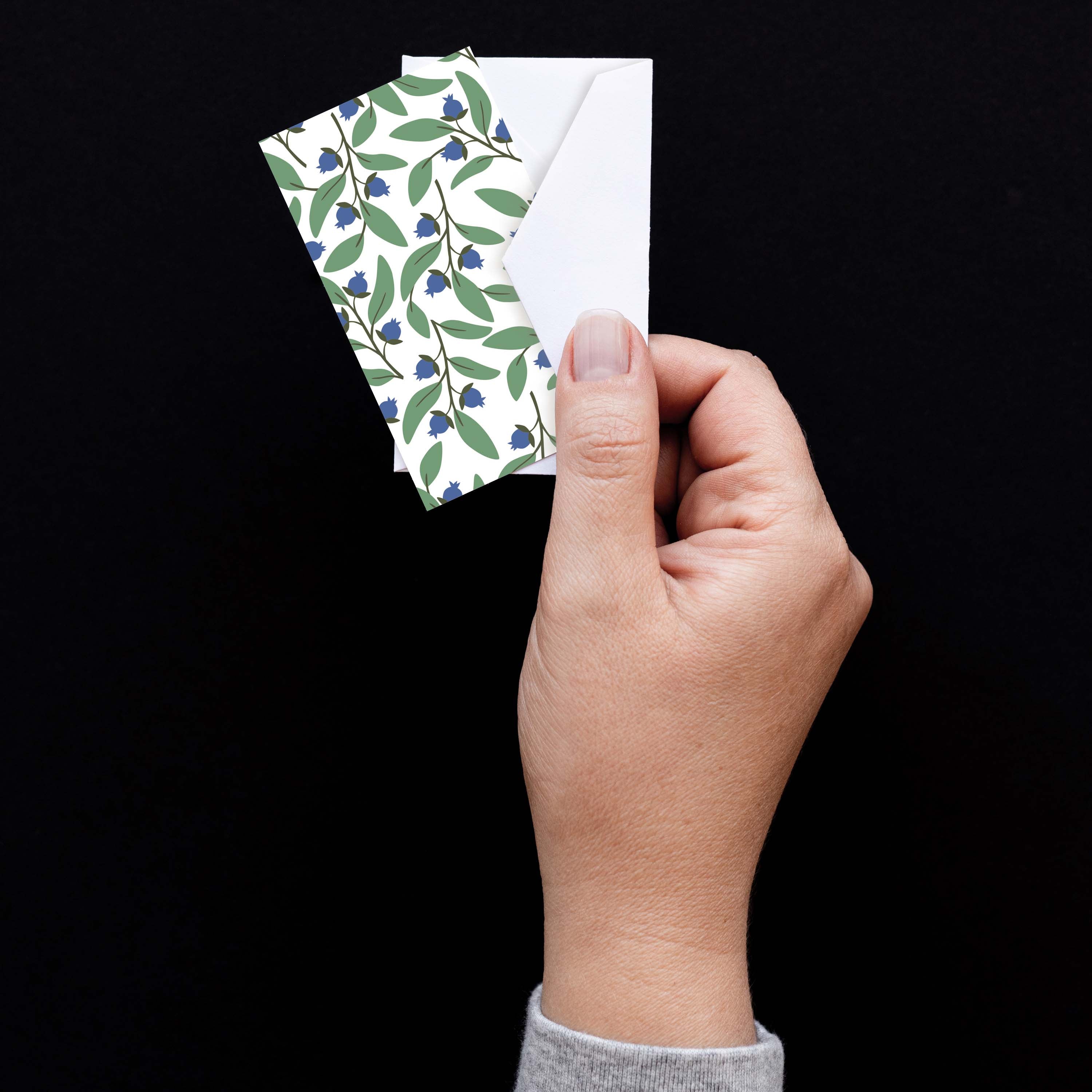 Hand holding a Blueberry Bushel Mini Note Card with a white envelope against a dark background