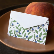 Blueberry Bushel Mini Note Card and envelope styled beside a peach on a brown plate