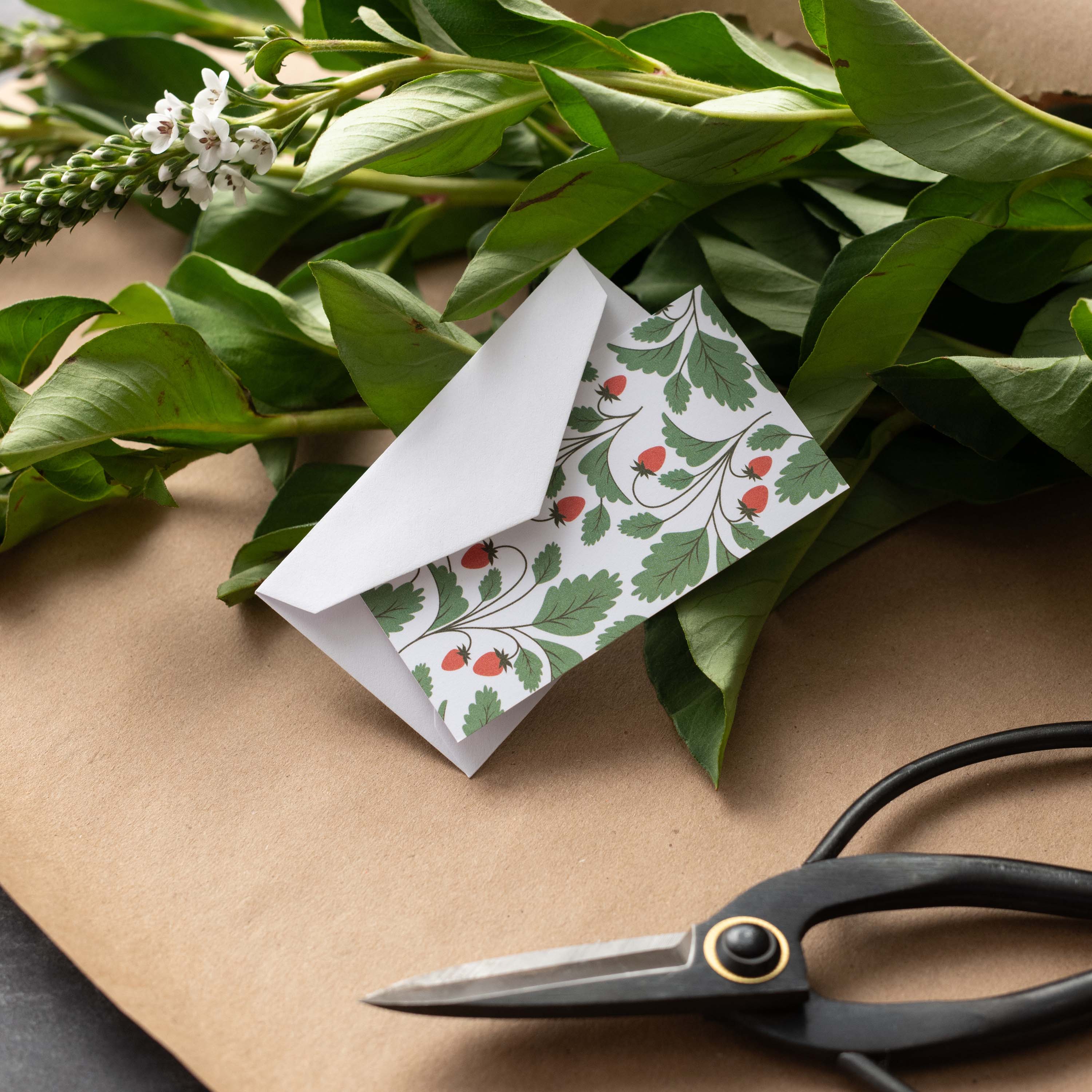 Wild Strawberries Mini Note Card styled with a white envelope, greenery, and scissors on kraft paper