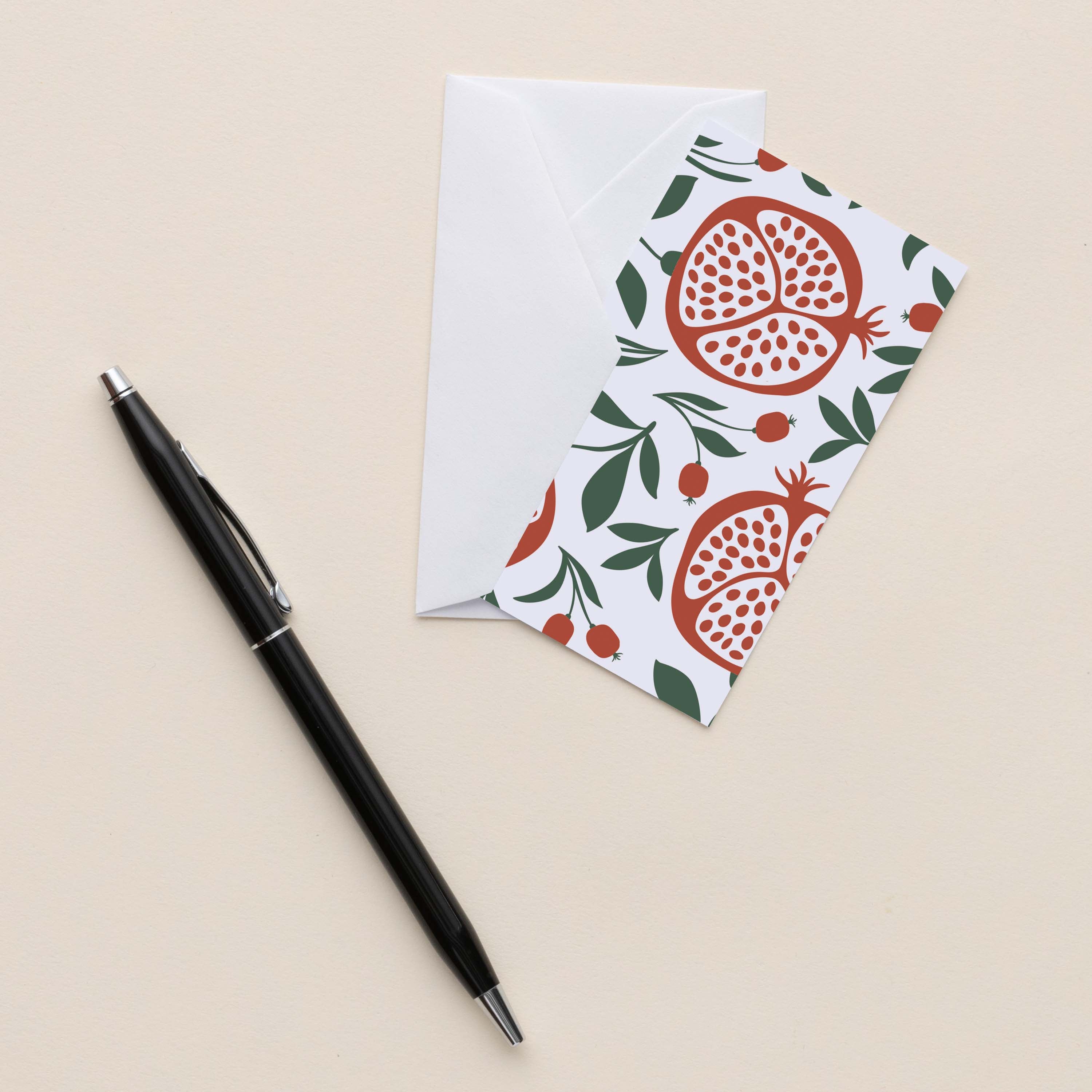 Pomegranates Mini Note Card with white envelope beside a black pen on a neutral background