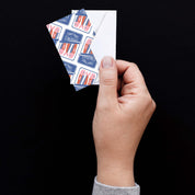Hand holding a Sardines Mini Note Card with a white envelope against a dark background