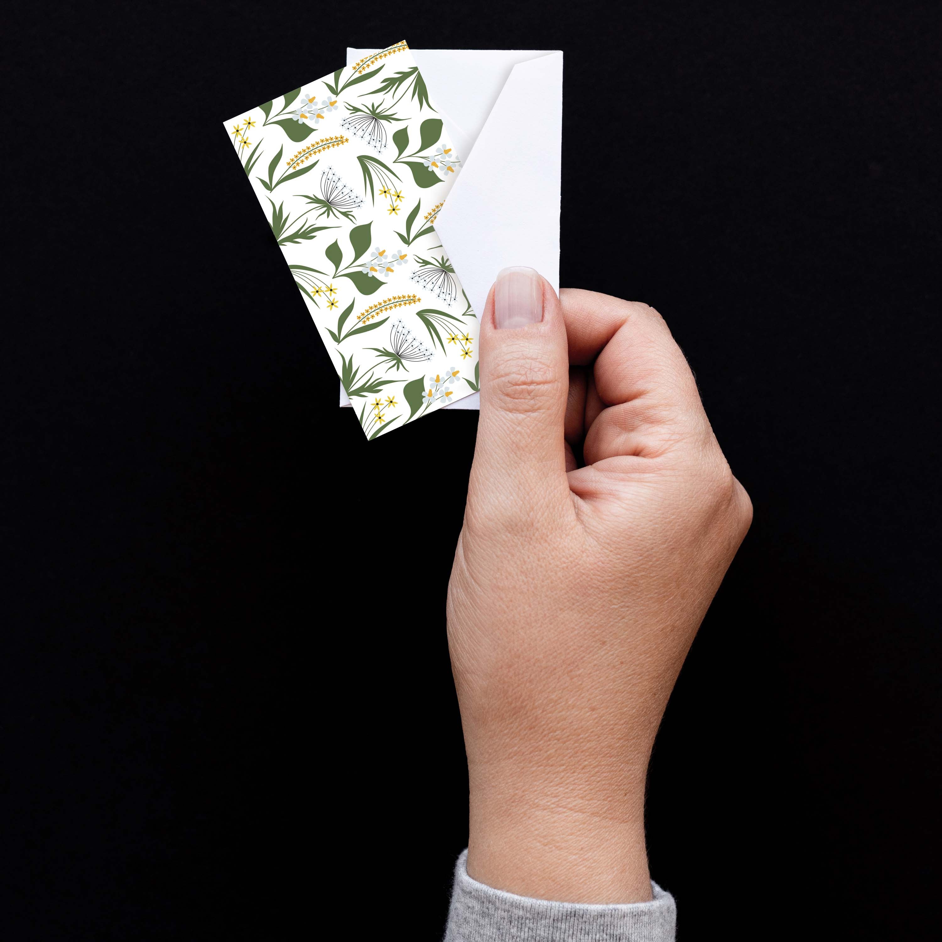 Hand holding a Wildflowers Mini Note Card with a white envelope against a dark background