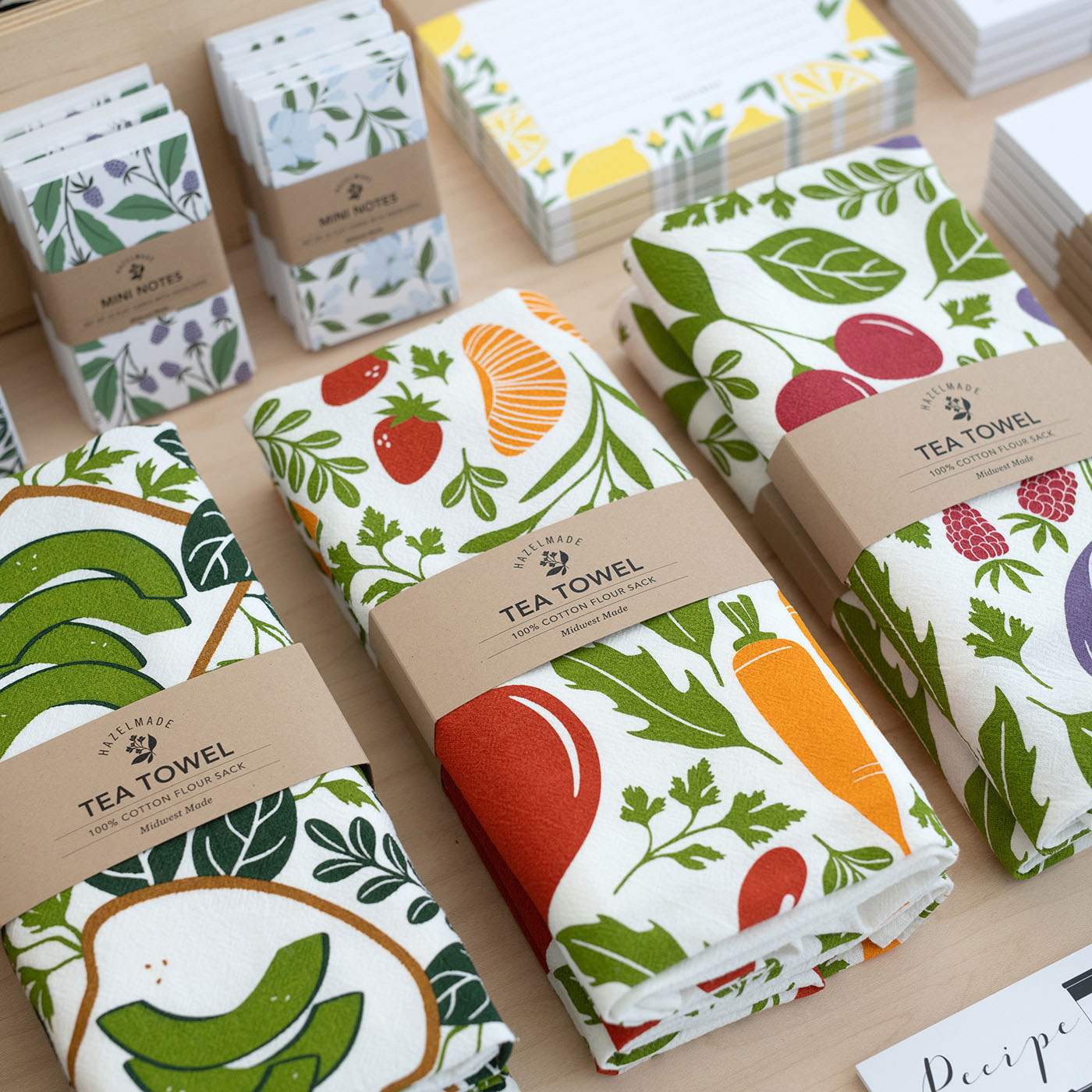 Assorted Hazelmade tea towels, mini notes, and paper goods arranged on display