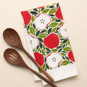 Harvest Apples Tea Towel with hand-illustrated apple design beside wooden kitchen utensils