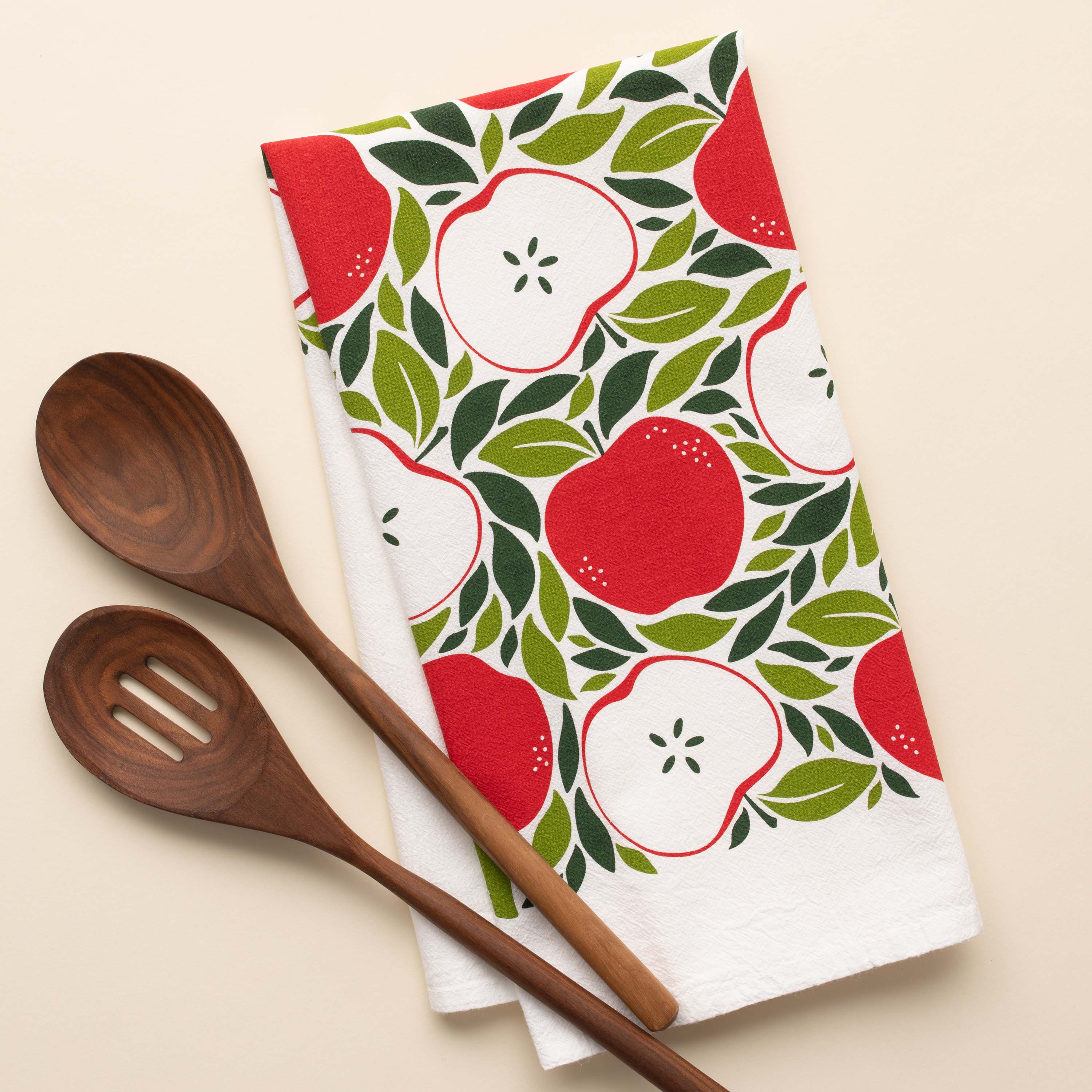 Harvest Apples Tea Towel with hand-illustrated apple design beside wooden kitchen utensils