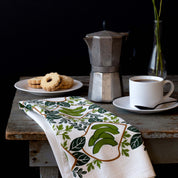 Avocado Toast Tea Towel draped over a table beside a moka pot, coffee cup, and pastries