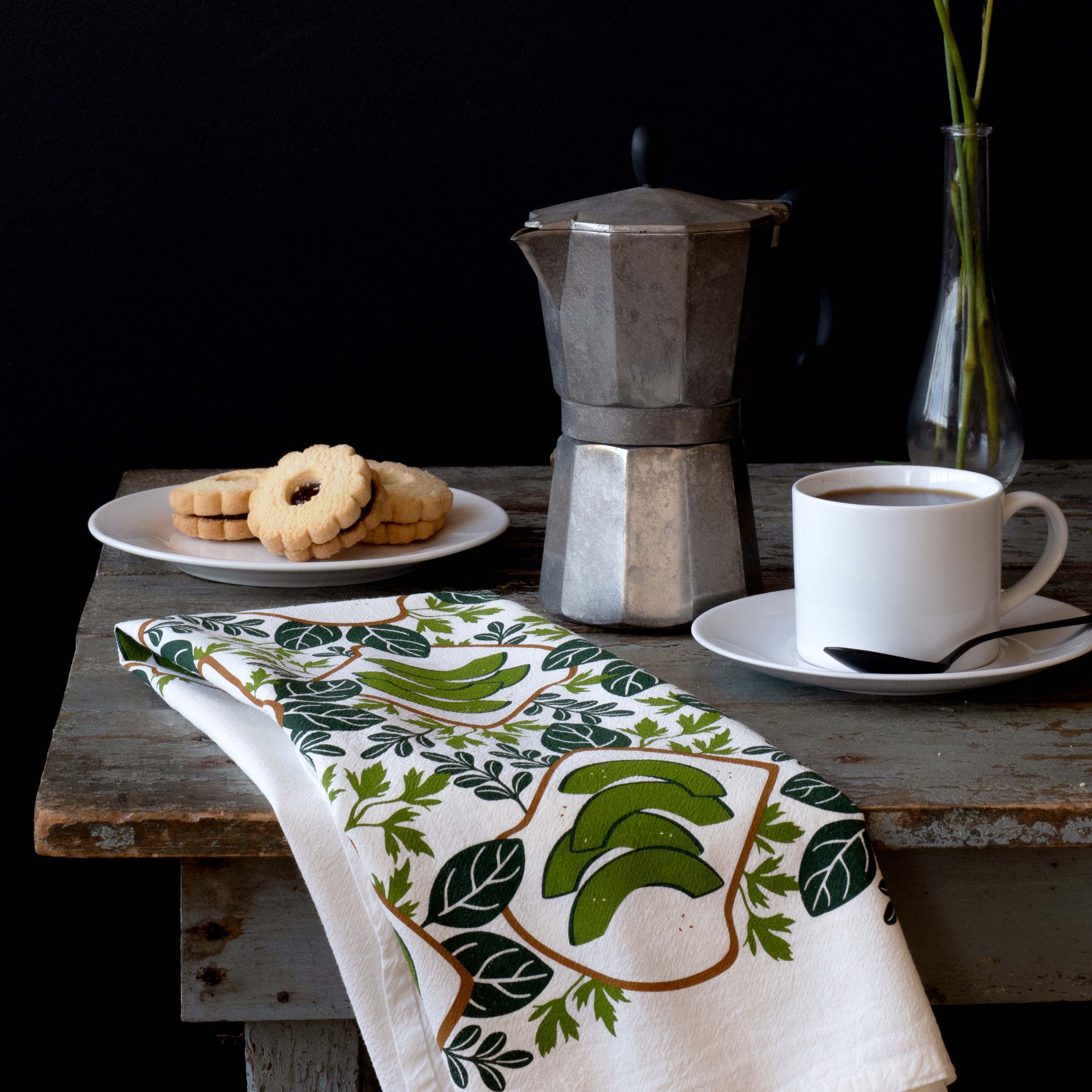 Avocado Toast Tea Towel draped over a table beside a moka pot, coffee cup, and pastries
