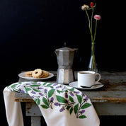 Blackberry Vines Tea Towel styled on a rustic table with coffee, pastries, and a flower vase