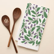 Blackberry Vines Tea Towel with hand-illustrated blackberry vine design beside wooden kitchen utensils
