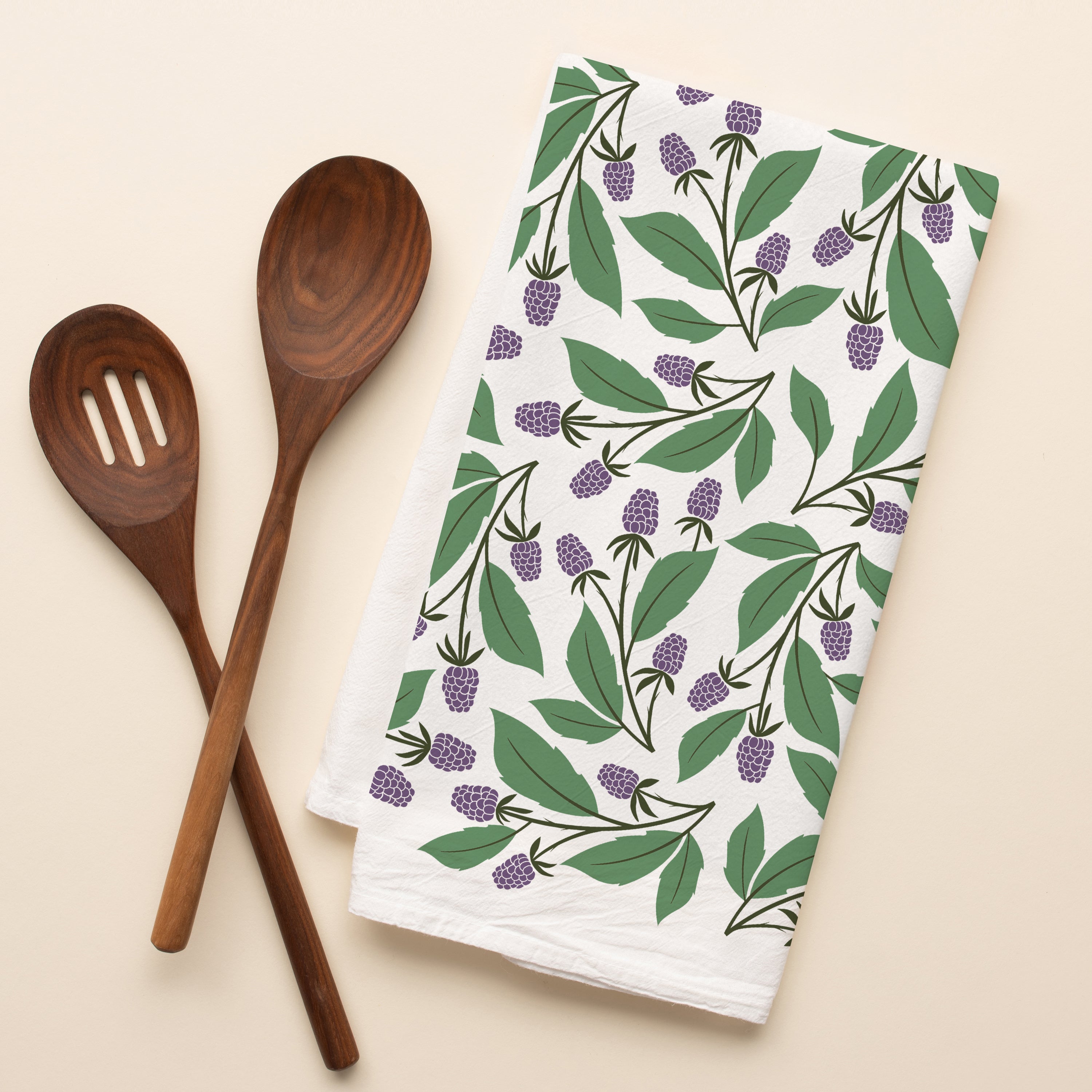 Blackberry Vines Tea Towel with hand-illustrated blackberry vine design beside wooden kitchen utensils
