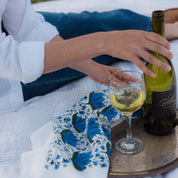 Blue Gentian Tea Towel styled beside a wine bottle and glass as a person pours a drink