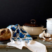 Blue Gentian Tea Towel draped over a table beside a Dutch oven, garlic, and bread