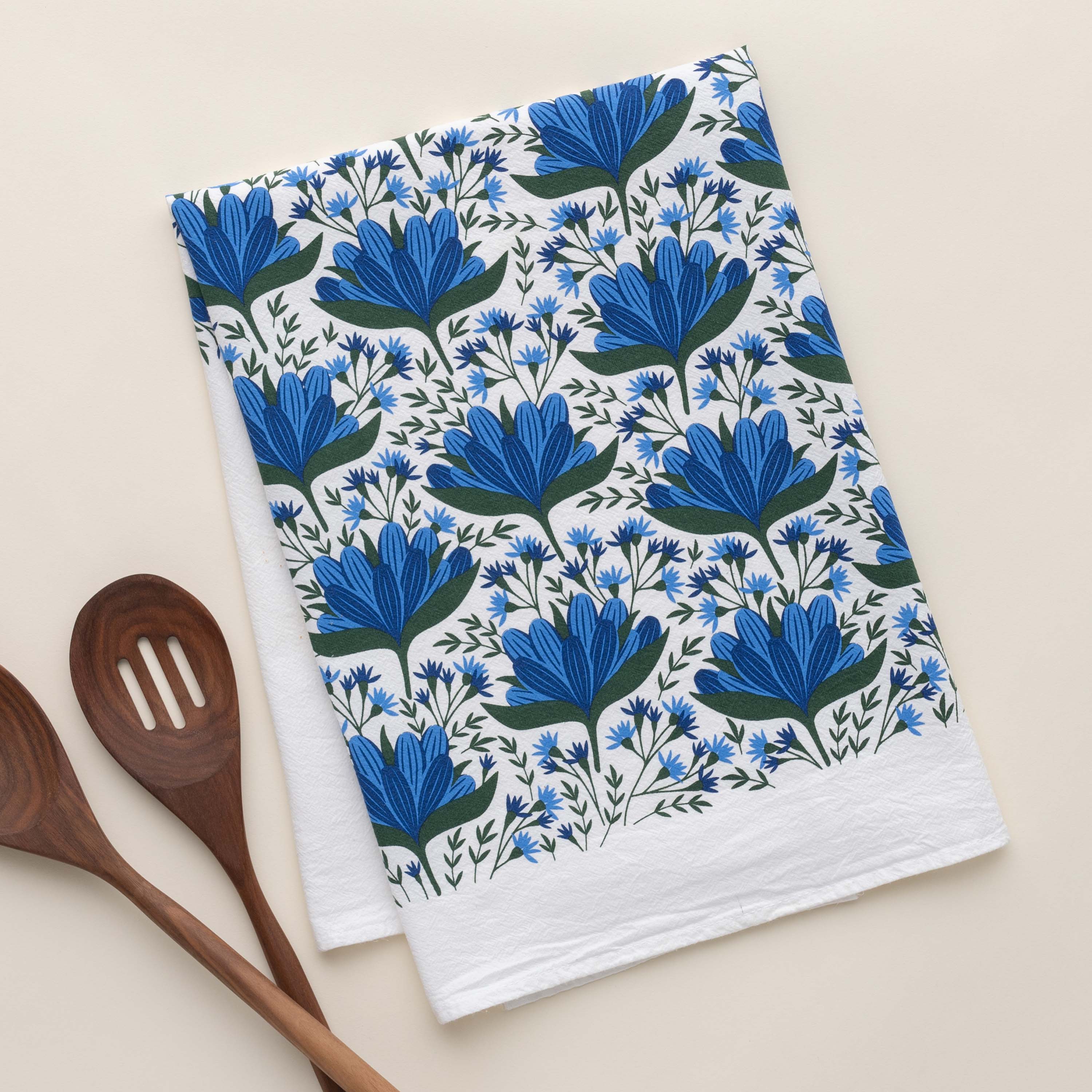 Blue Gentian Tea Towel with hand-illustrated blue floral design beside wooden kitchen utensils