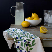 Blueberry Bushel Tea Towel styled beside lemons and a glass pitcher on a rustic table