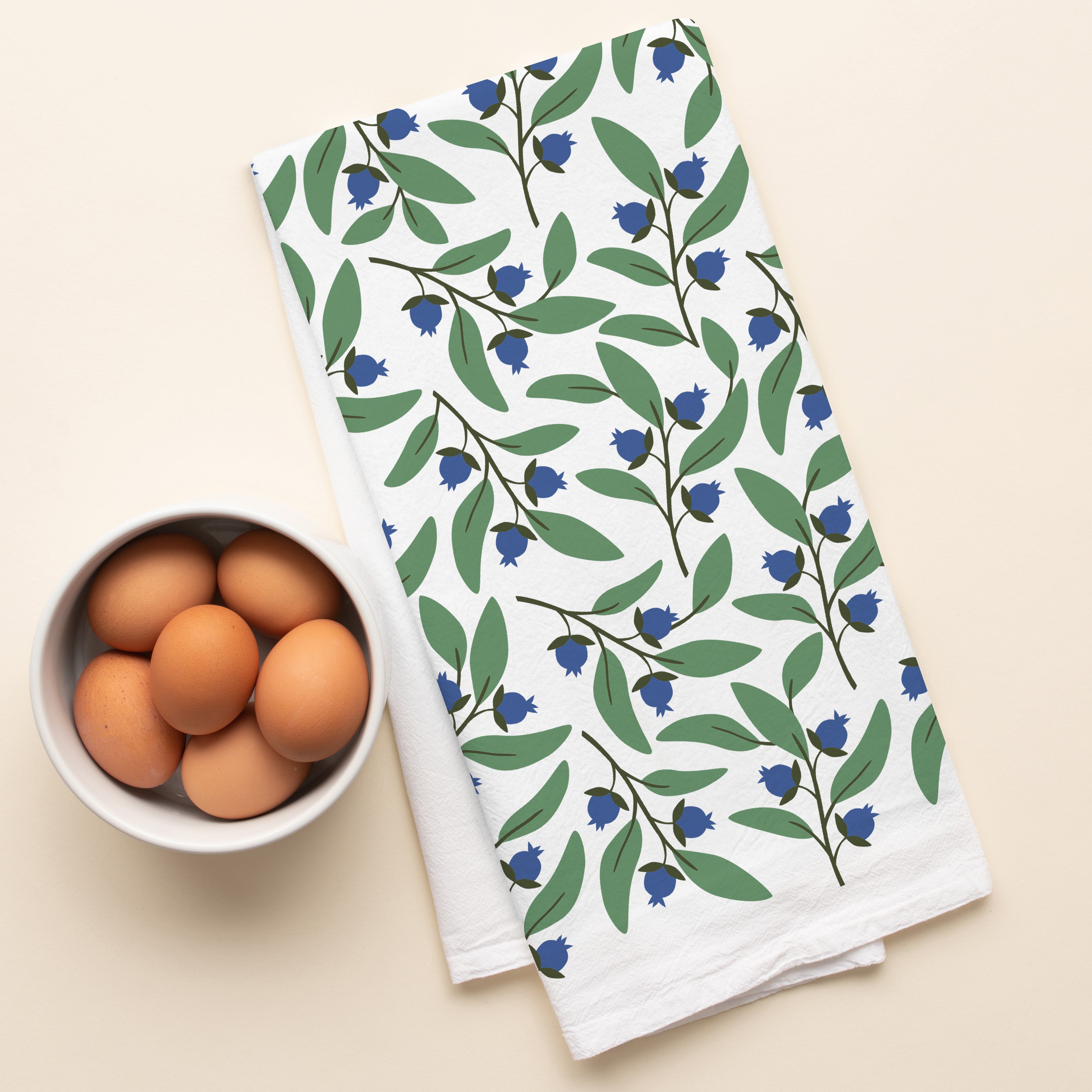 Blueberry Bushel Tea Towel with hand-illustrated blueberry design beside a bowl of brown eggs