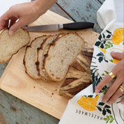 Breakfast Diner Tea Towel wrapped around sliced bread on a cutting board while a person slices the loaf