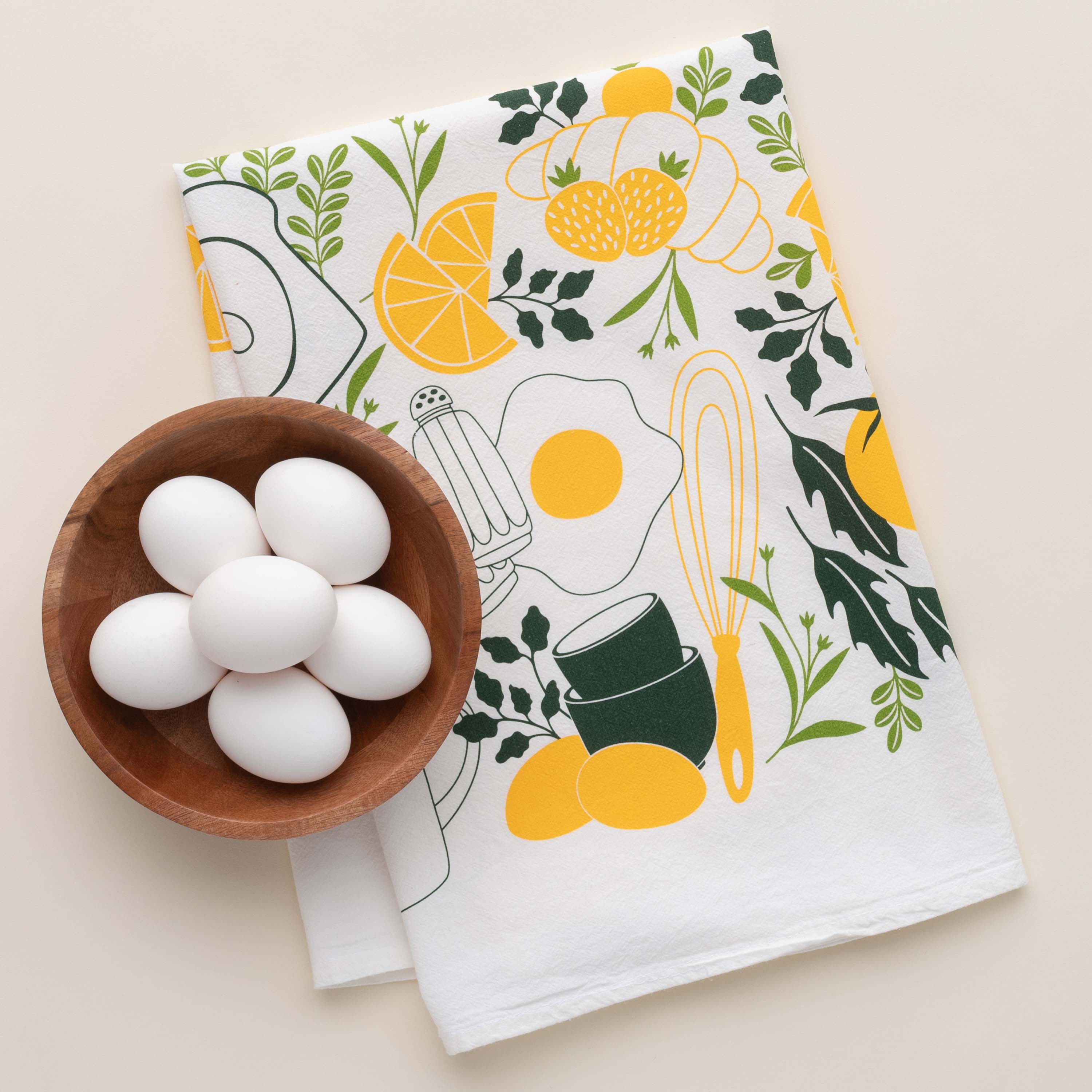 Breakfast Diner Tea Towel with hand-illustrated breakfast food design beside a bowl of white eggs