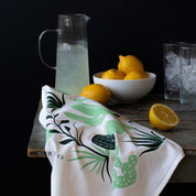 Cactus Tea Towel draped over a wooden table beside a pitcher of lemonade and lemons