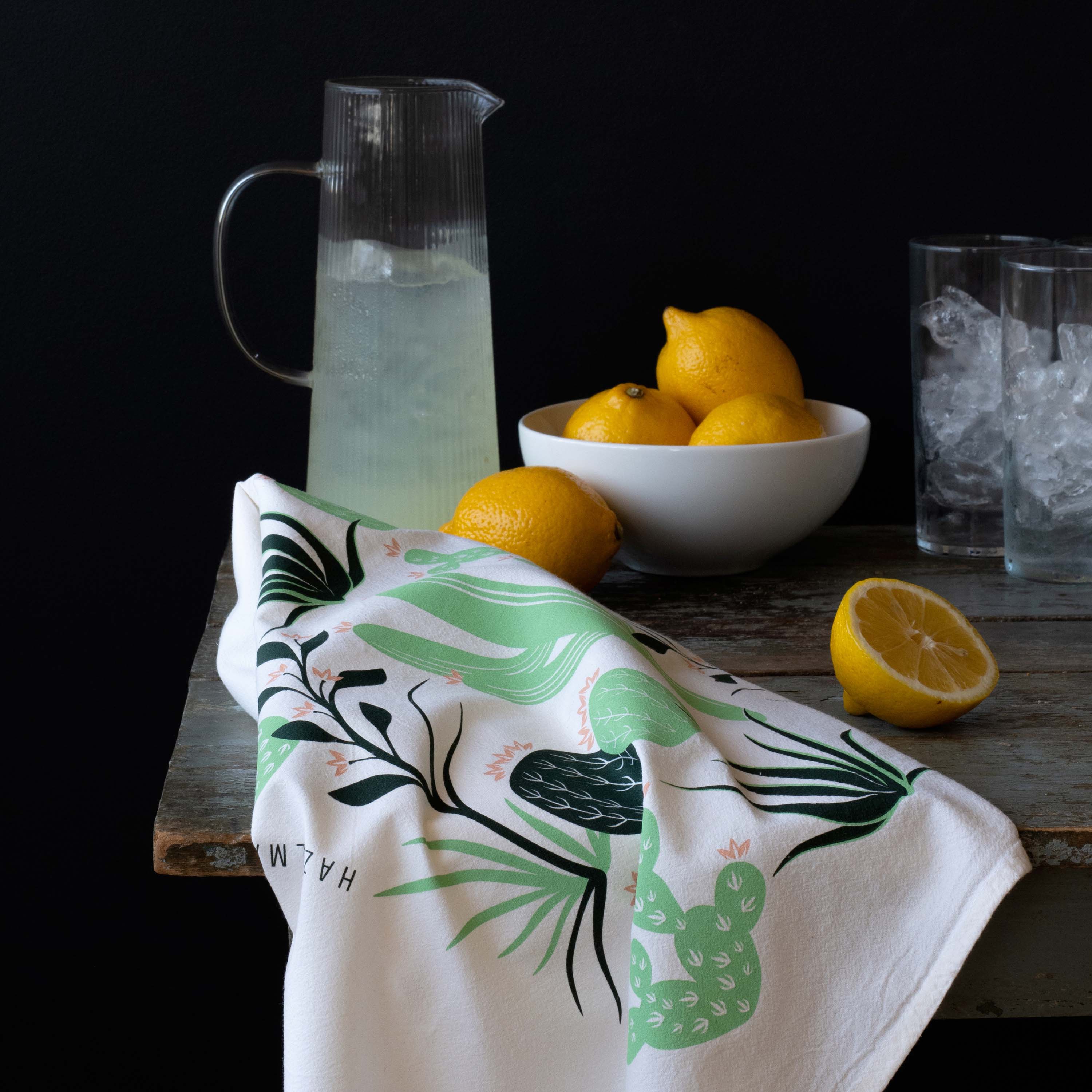 Cactus Tea Towel draped over a wooden table beside a pitcher of lemonade and lemons